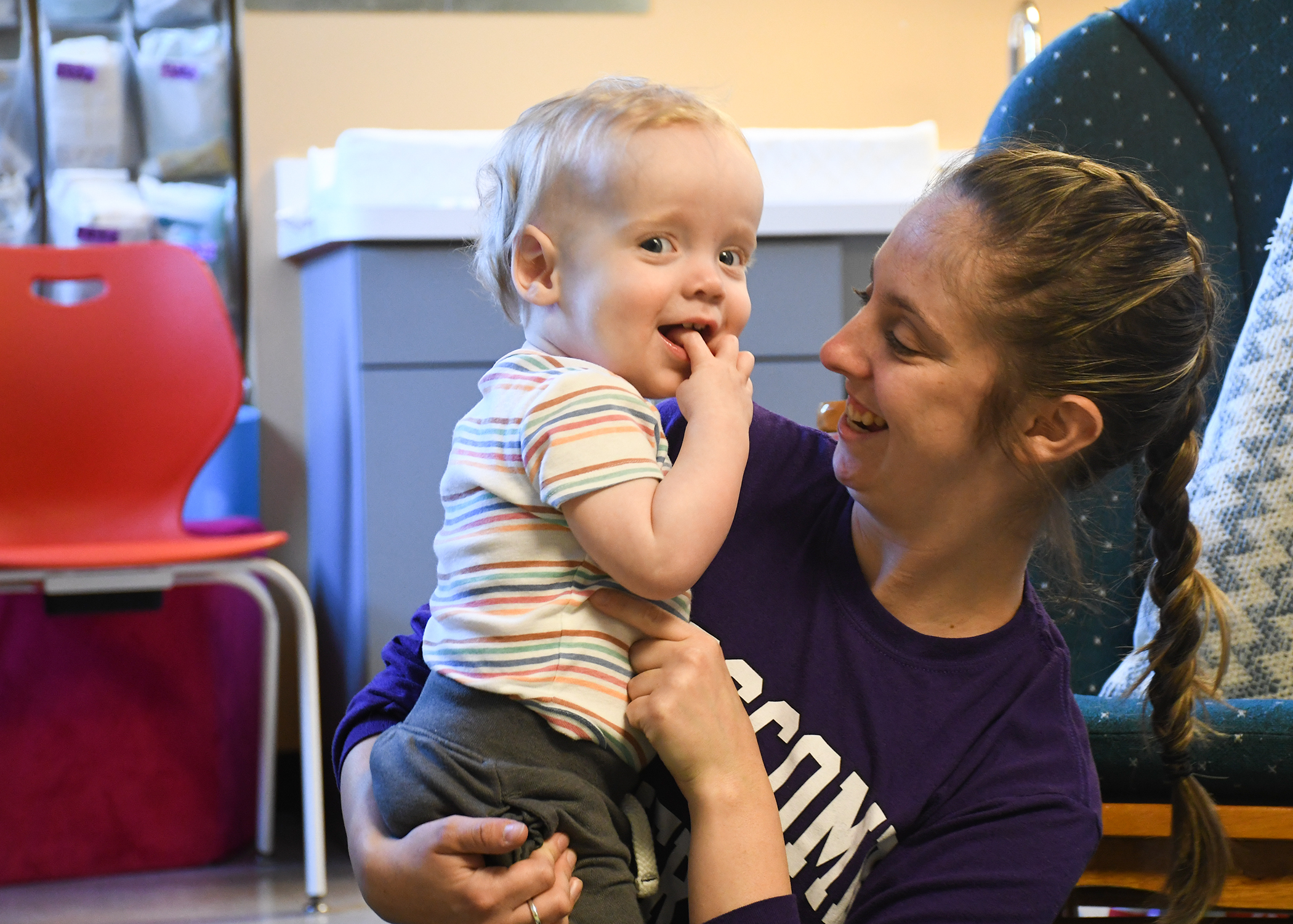 White child care teacher holding a white, blonde toddler. Both are smiling.