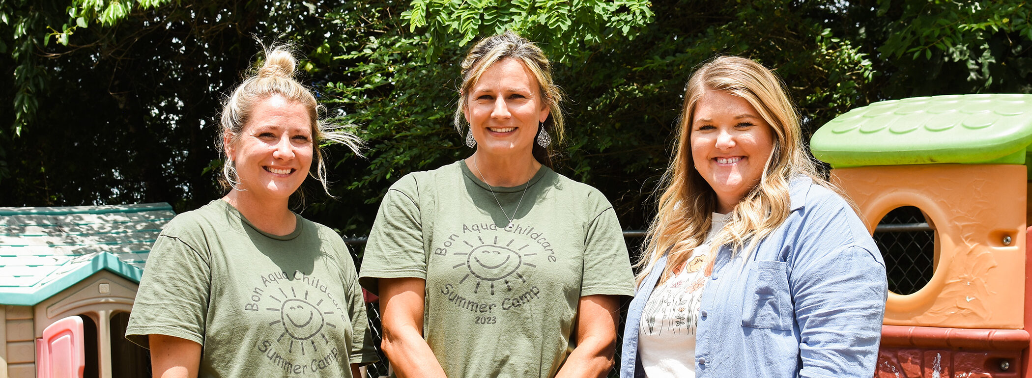 Three white female child care providers standing on the playground smiling.