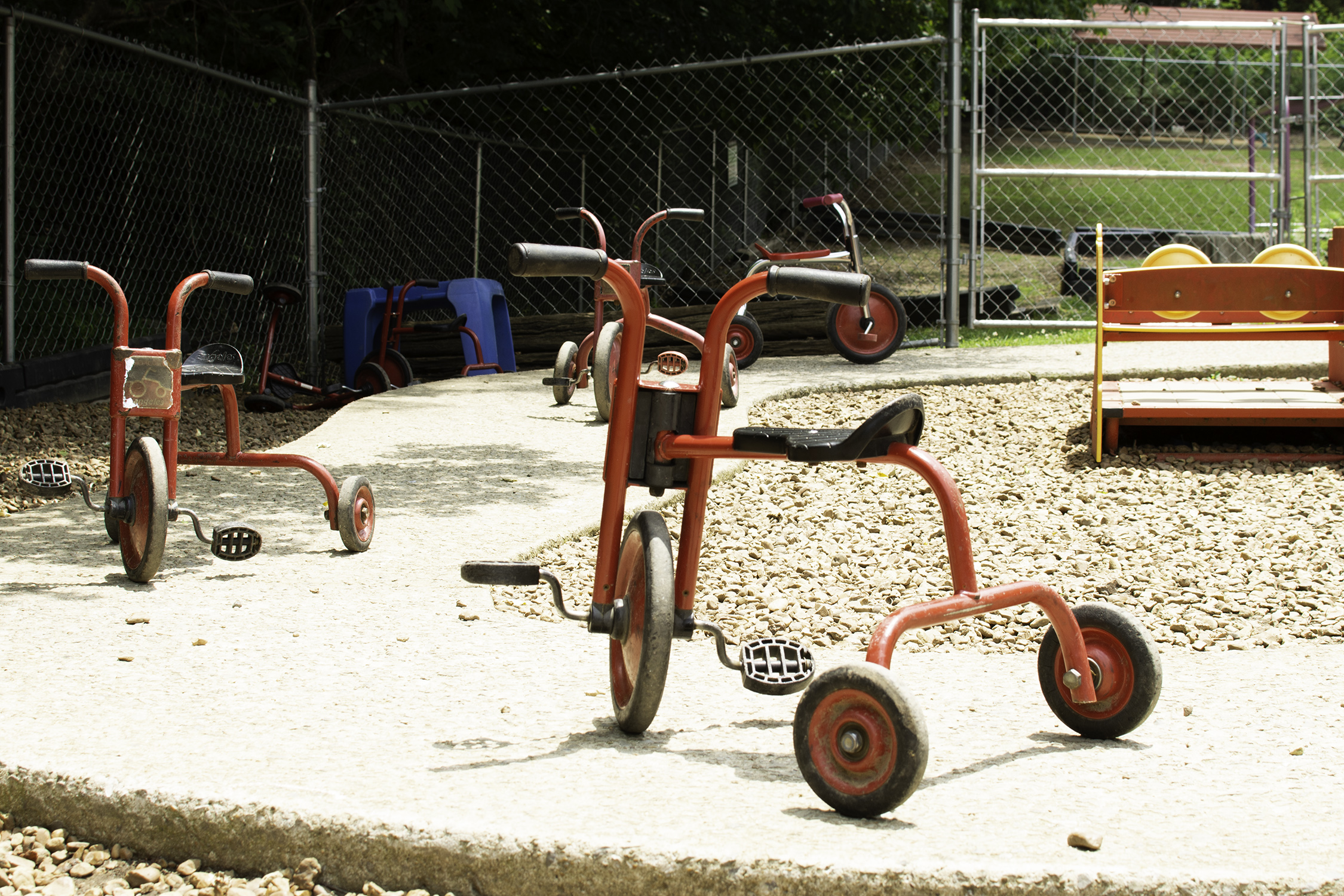 Red tricycles sit on a concrete track in the middle of a playground at a child care center.